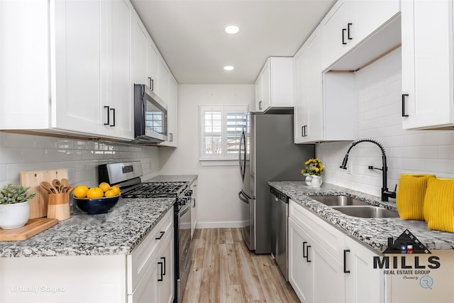 kitchen featuring appliances with stainless steel finishes, light stone countertops, sink, and white cabinets