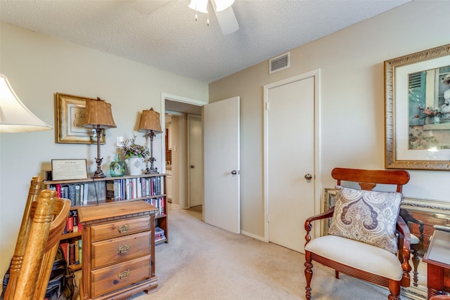 sitting room featuring ceiling fan, a textured ceiling, and light carpet