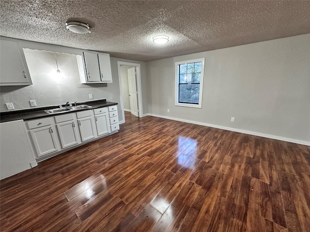 708 Ellington St, Atlanta, TX 75551 - kitchen featuring a sink, a textured ceiling, dark wood finished floors, dark countertops, and baseboards