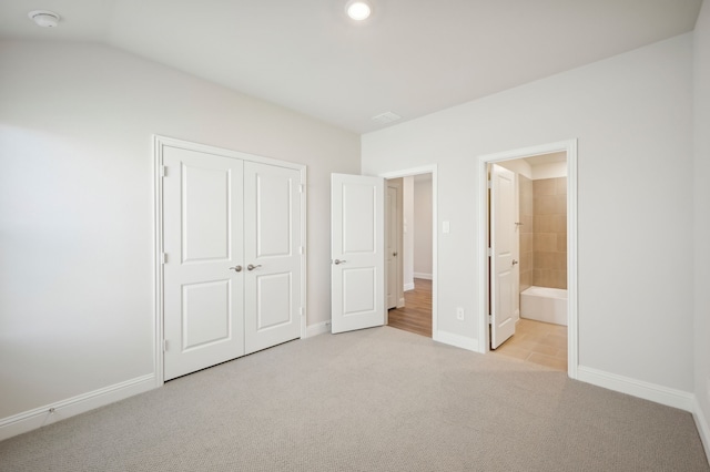 unfurnished bedroom with ensuite bathroom, a closet, light colored carpet, and lofted ceiling