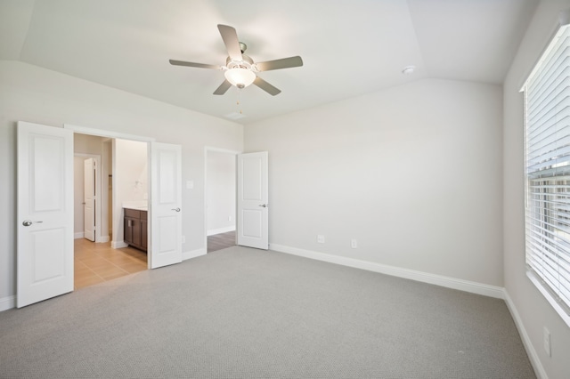 unfurnished bedroom featuring vaulted ceiling, light colored carpet, ensuite bath, and ceiling fan