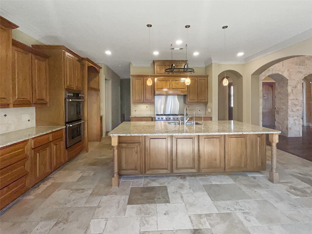 kitchen with sink, decorative light fixtures, a large island with sink, stainless steel double oven, and backsplash