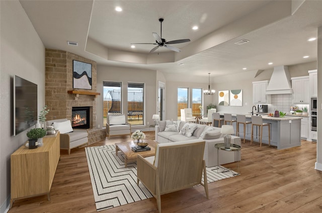 living area with visible vents, a stone fireplace, light wood-style flooring, and ceiling fan with notable chandelier