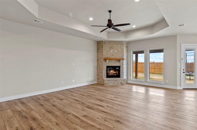 unfurnished living room featuring light wood-style floors, a raised ceiling, a ceiling fan, and visible vents