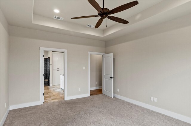 unfurnished bedroom featuring a raised ceiling, baseboards, light colored carpet, and visible vents