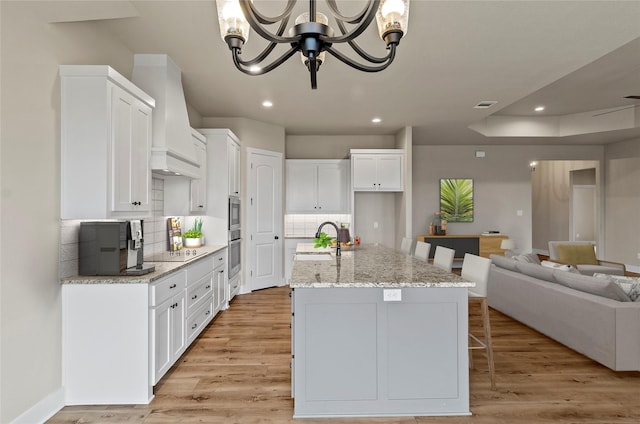 kitchen with an inviting chandelier, black electric stovetop, a sink, open floor plan, and custom exhaust hood