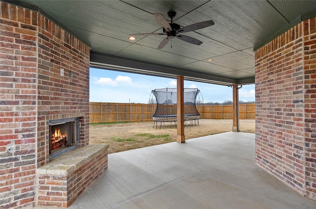 view of patio featuring ceiling fan, a fenced backyard, a trampoline, and an outdoor brick fireplace