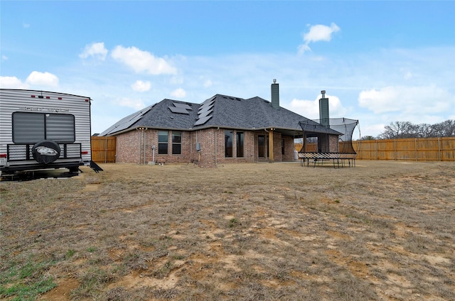 rear view of house with brick siding, solar panels, a fenced backyard, and a chimney