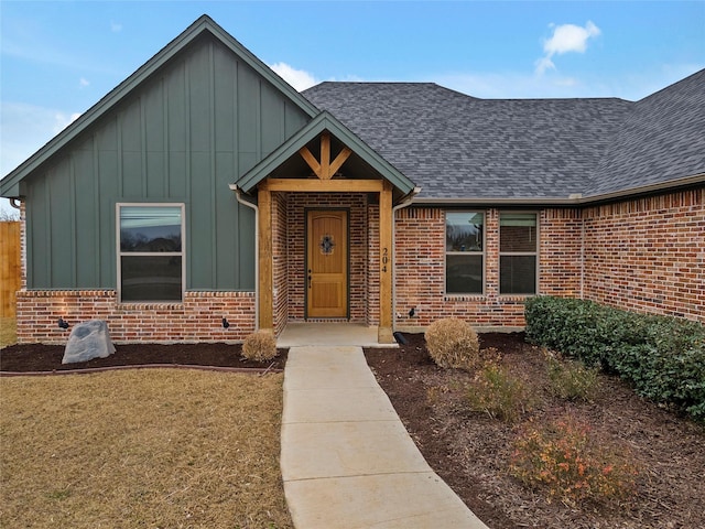 view of front facade featuring a shingled roof, board and batten siding, and brick siding