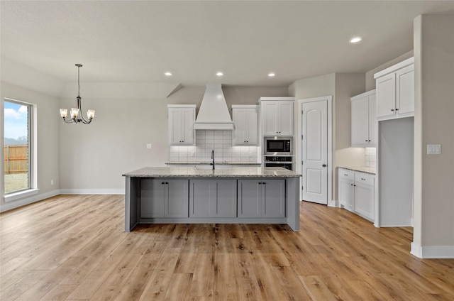kitchen with decorative backsplash, oven, premium range hood, built in microwave, and white cabinets