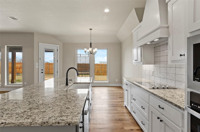 kitchen featuring visible vents, premium range hood, a sink, light wood-style flooring, and vaulted ceiling