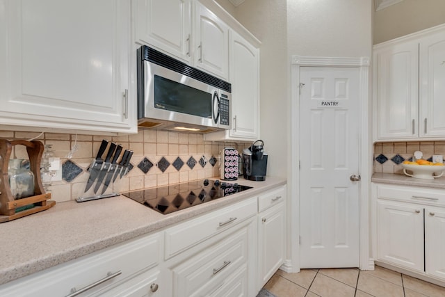 kitchen with black electric stovetop, decorative backsplash, white cabinetry, and light tile patterned floors