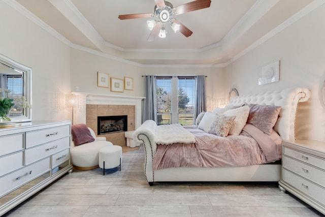 bedroom with a tray ceiling, a tile fireplace, ceiling fan, and crown molding