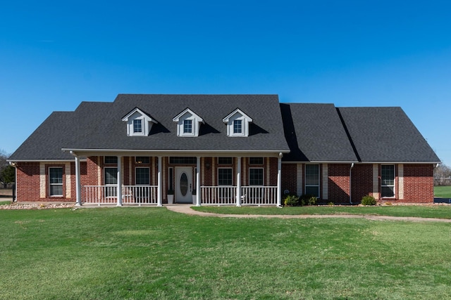 cape cod house with a porch, a front yard, brick siding, and roof with shingles