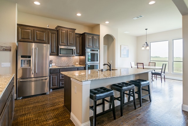 kitchen featuring stainless steel appliances, a kitchen island with sink, a breakfast bar, and tasteful backsplash