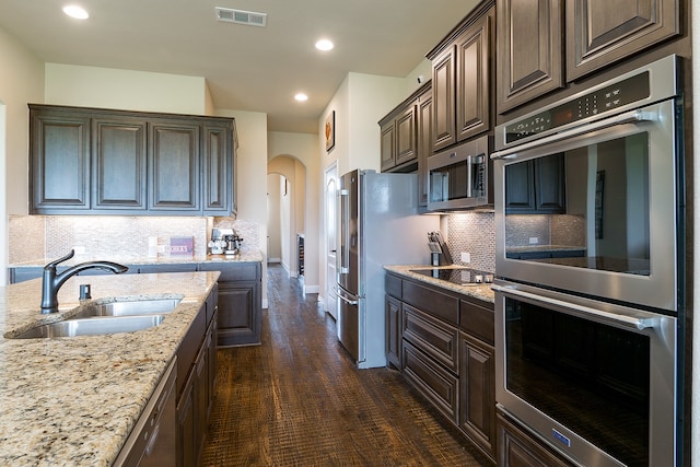 kitchen with sink, tasteful backsplash, dark brown cabinetry, dark hardwood / wood-style flooring, and appliances with stainless steel finishes