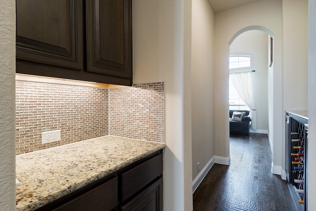 kitchen featuring light stone countertops, dark wood-type flooring, dark brown cabinets, and decorative backsplash