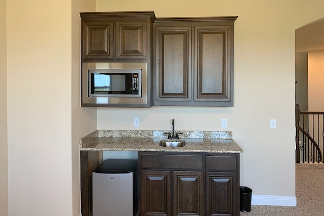 kitchen with sink, fridge, stainless steel microwave, and light stone counters