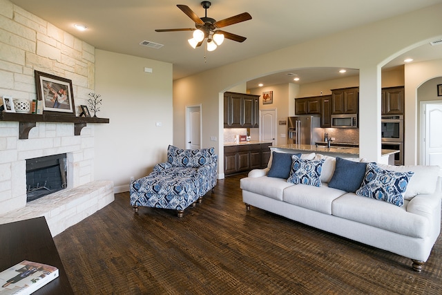 living room featuring a stone fireplace, ceiling fan, and dark hardwood / wood-style floors