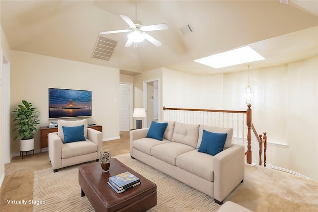 carpeted living room with ceiling fan and vaulted ceiling with skylight