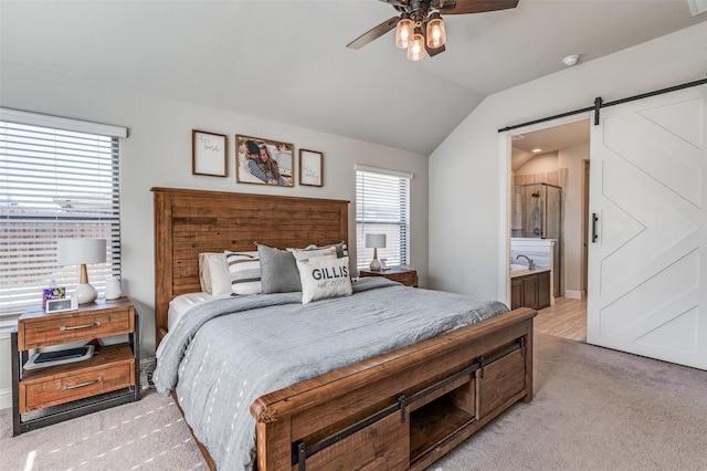 carpeted bedroom featuring a barn door, ensuite bathroom, ceiling fan, and vaulted ceiling