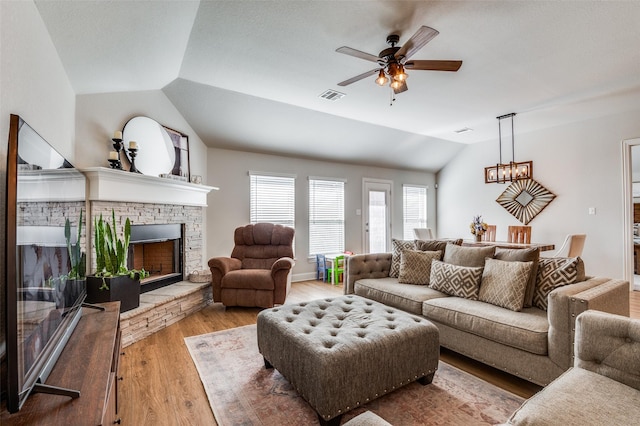 living room featuring a fireplace, hardwood / wood-style floors, ceiling fan with notable chandelier, and vaulted ceiling