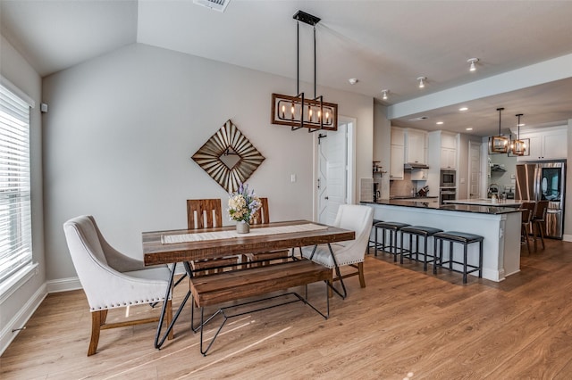 dining space with sink, vaulted ceiling, and light wood-type flooring