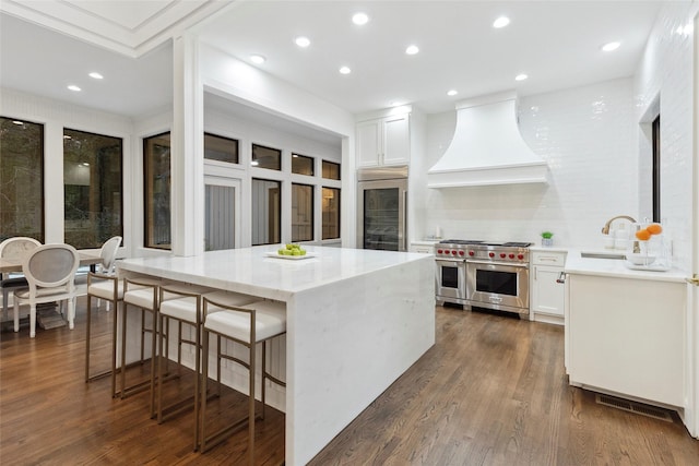 kitchen featuring custom exhaust hood, sink, double oven range, white cabinets, and a kitchen island