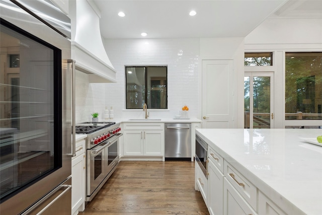 kitchen with backsplash, sink, custom range hood, white cabinetry, and stainless steel appliances