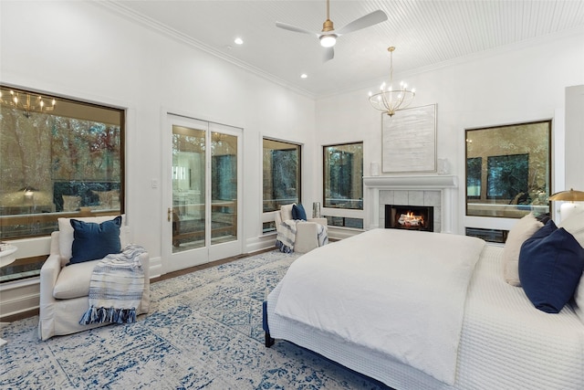 bedroom with access to outside, a tiled fireplace, crown molding, and ceiling fan with notable chandelier