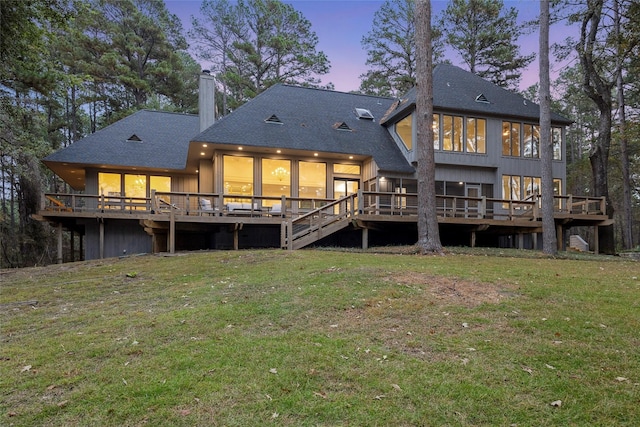 back house at dusk with a lawn and a wooden deck