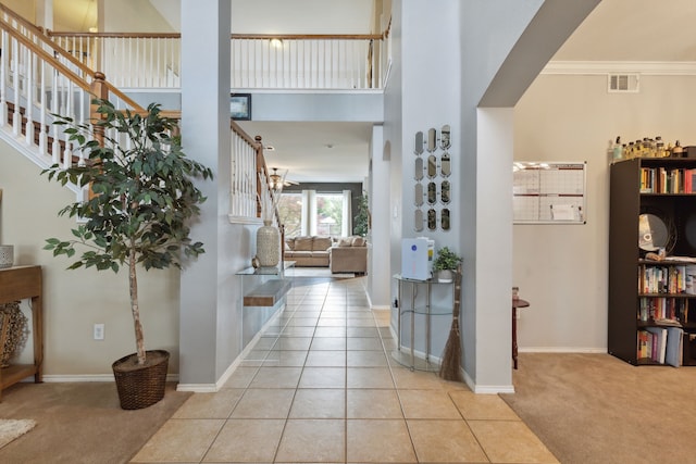 tiled entryway with ceiling fan, ornamental molding, and a high ceiling