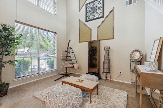 sitting room featuring carpet flooring, plenty of natural light, and a towering ceiling