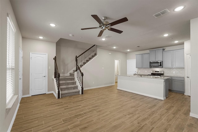 kitchen with appliances with stainless steel finishes, tasteful backsplash, gray cabinetry, ceiling fan, and a center island with sink