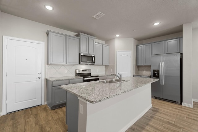 kitchen with light stone countertops, gray cabinetry, stainless steel appliances, sink, and a center island with sink