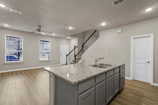 kitchen featuring ceiling fan, light stone counters, sink, and a kitchen island with sink