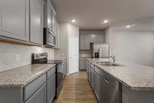 kitchen with light stone countertops, sink, gray cabinets, a center island with sink, and appliances with stainless steel finishes