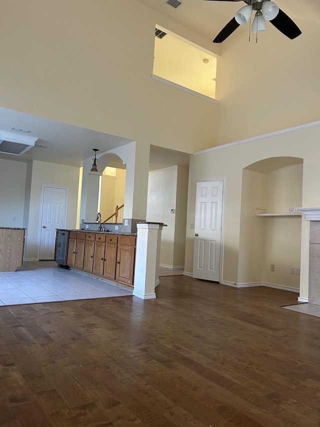 unfurnished living room featuring a towering ceiling, ceiling fan, sink, light hardwood / wood-style flooring, and a tiled fireplace