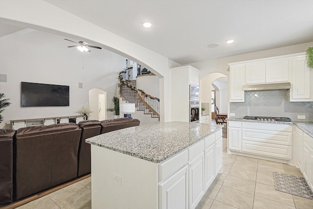 kitchen featuring light stone countertops, white cabinets, appliances with stainless steel finishes, a kitchen island, and ceiling fan