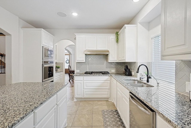 kitchen with light tile patterned floors, white cabinetry, appliances with stainless steel finishes, light stone counters, and sink