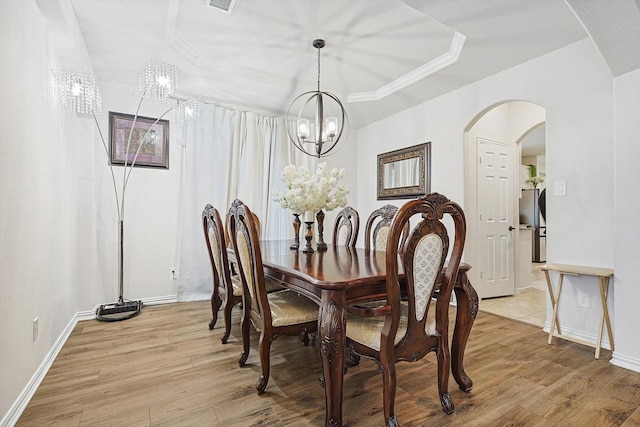 dining area with a notable chandelier, a tray ceiling, and light hardwood / wood-style flooring