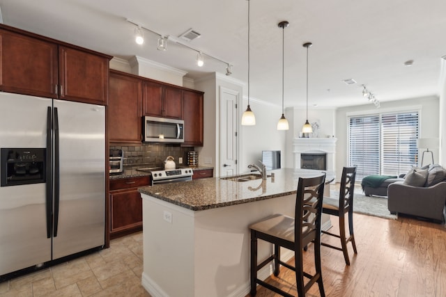 kitchen featuring a breakfast bar, tasteful backsplash, dark stone countertops, an island with sink, and stainless steel appliances