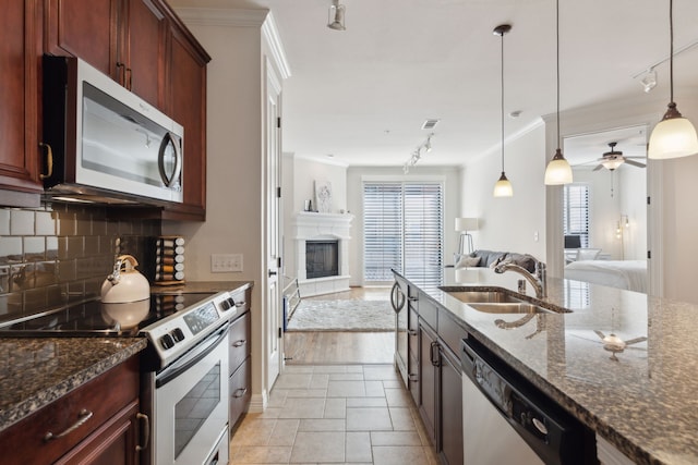 kitchen featuring a fireplace with raised hearth, open floor plan, decorative backsplash, appliances with stainless steel finishes, and a sink