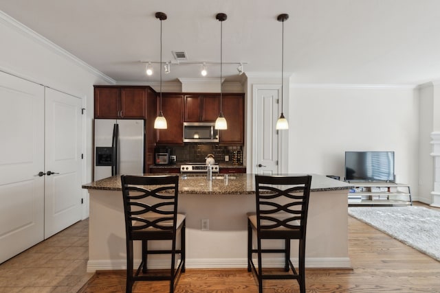 kitchen with appliances with stainless steel finishes, dark stone counters, a kitchen island with sink, and a breakfast bar area