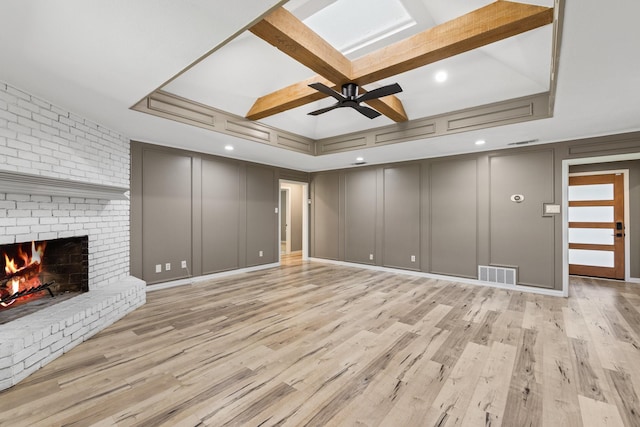 unfurnished living room featuring ceiling fan, a fireplace, light hardwood / wood-style floors, and coffered ceiling