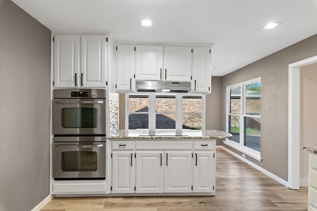 kitchen featuring light stone countertops, black electric stovetop, light wood-type flooring, stainless steel double oven, and white cabinets