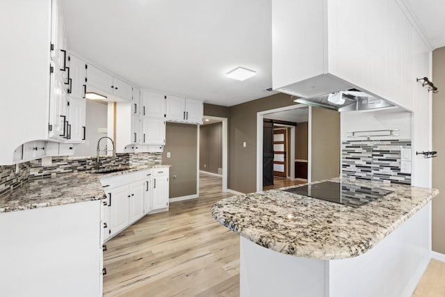 kitchen featuring black electric stovetop, light stone counters, custom range hood, sink, and white cabinets