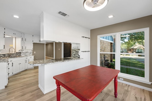 kitchen with light stone countertops, decorative backsplash, kitchen peninsula, sink, and white cabinetry