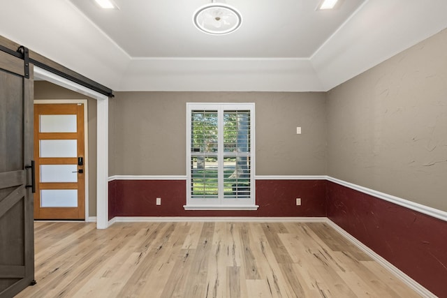 spare room featuring a barn door, a tray ceiling, and light hardwood / wood-style floors