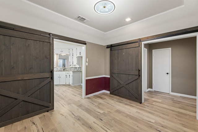 interior space with sink, a barn door, decorative backsplash, white cabinets, and light wood-type flooring